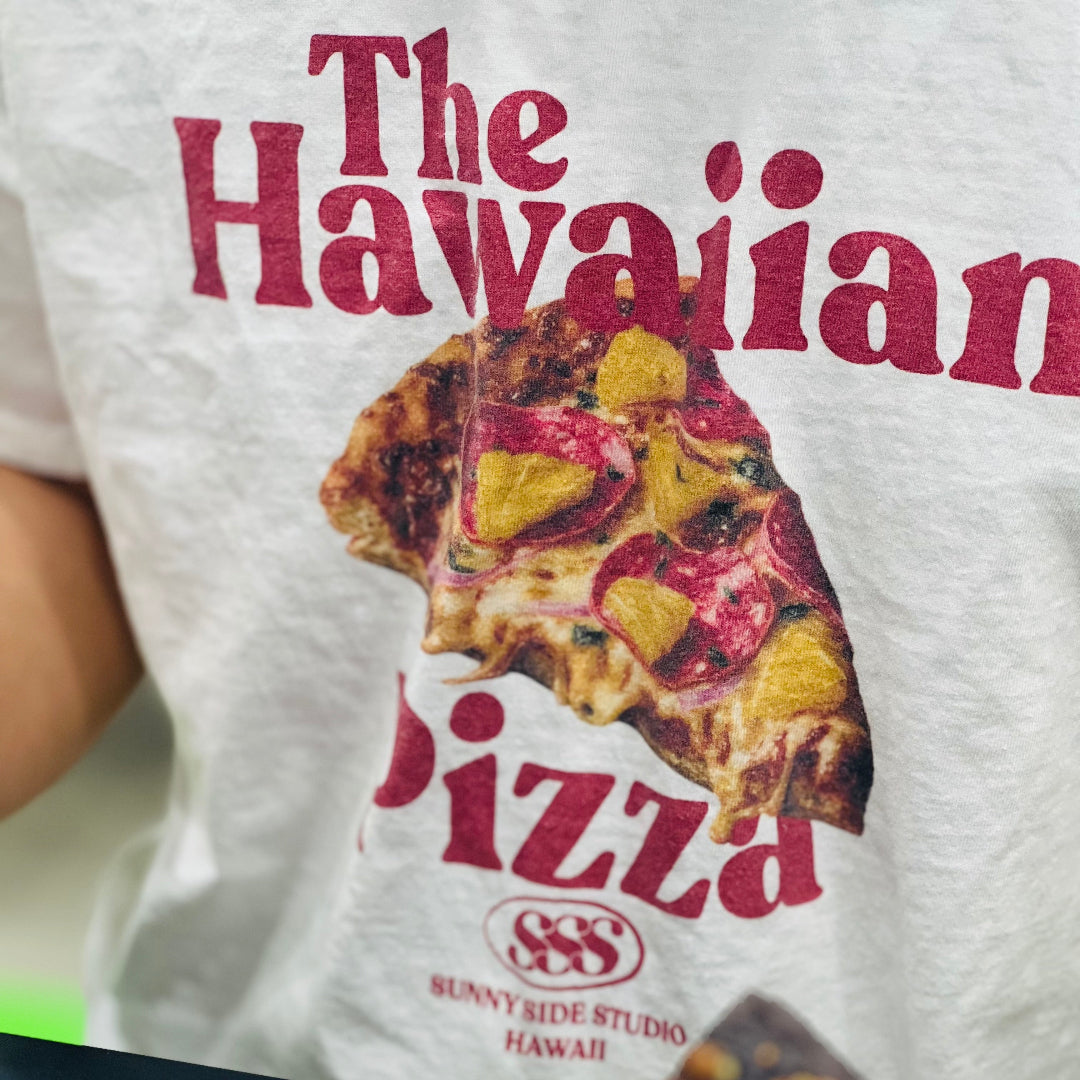 Person wearing a t-shirt with a pizza design and text, holding a slice of pizza.