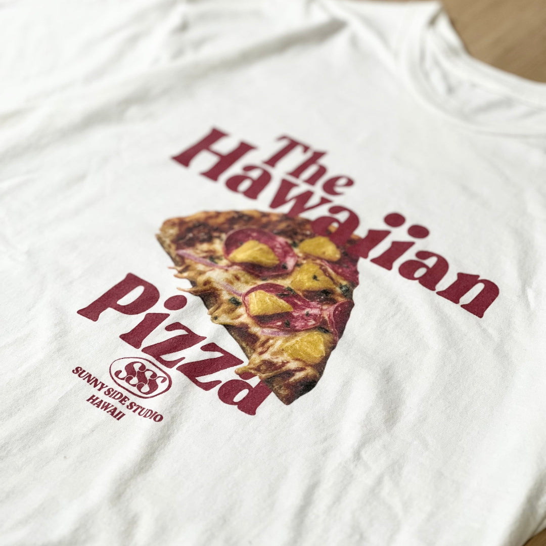 White t-shirt with 'The Hawaiian Pizza' graphic design on a wooden surface