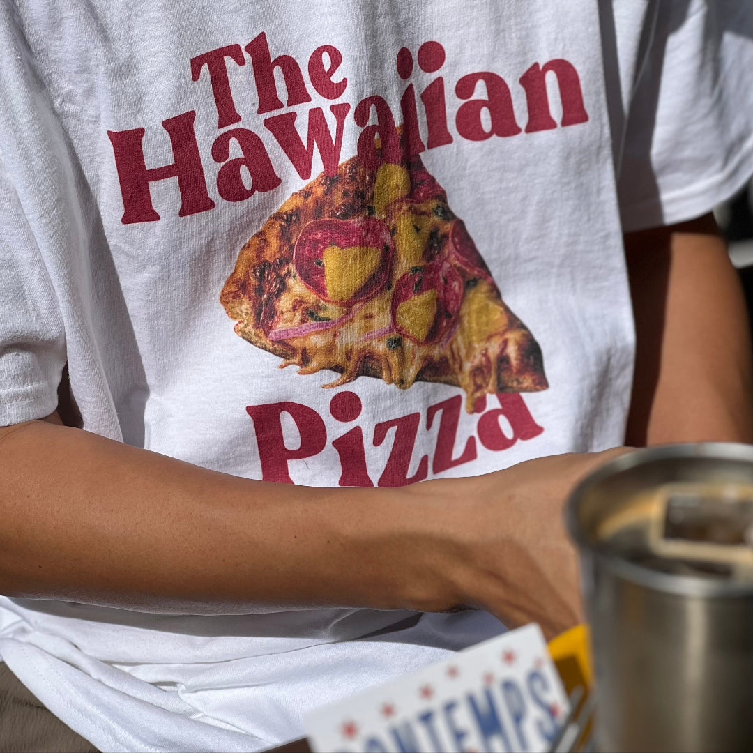 Person wearing a white t-shirt with 'The Hawaiian Pizza' graphic design.